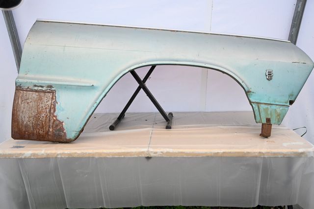 Classic front fender on a backdrop, with surface rust on the lower rear corner