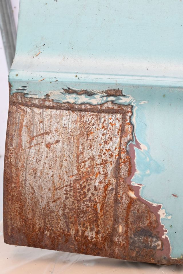 Close-up of surface rust and worn paint on the lower corner of a front fender