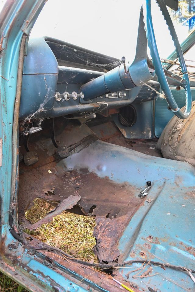Rusted-through driver's floor pan and cobwebbed dash inside a project car
